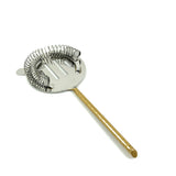 Metal cocktail strainer with a round perforated flat plate, coiled spring edge, and a slim golden handle, shown against a white background.