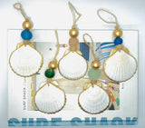 Six white scallop shells with gold-painted edges, each suspended by natural twine and adorned with colorful beads in blue, green, and gold above a SURF SHACK box.