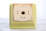 Square yellow ceramic bonsai pot shown upside down, featuring a central drainage hole and multiple smaller holes arranged in a circular pattern on the unglazed base.