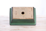 Rectangular bonsai pot viewed from the bottom, featuring a green glazed exterior and a beige unglazed base with a central drainage hole and small side holes.