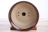 Round ceramic bonsai pot with smooth beige interior and glossy dark brown rim, featuring multiple drainage holes and resting on a wooden stand.