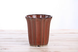 Tall ceramic bonsai pot with vertical ridges and a glossy rust-colored glaze, shown from the front on a light wooden surface.