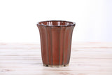 Rust-colored ceramic bonsai pot with vertical ridges and a slightly flared rim, shown on a light wooden surface with a white background.