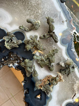 Greenish-brown stilbite crystal clusters arranged on a polished agate slice with layered gray, white, and dark blue bands and jagged edges.