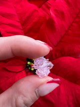 Small translucent pink rose quartz crystal cluster held between thumb and forefinger against vivid red poinsettia petals in the background.