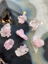 Seven small, translucent pink rose quartz crystals with jagged shapes arranged on a polished, multicolored agate surface featuring black, white, and blue-gray bands and a triangle-shaped hollow area.