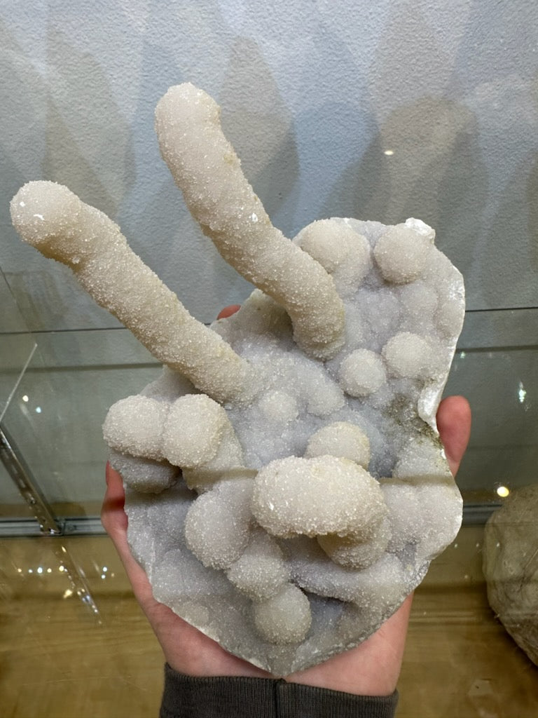 Hand holding a pale gray chalcedony stalactite cluster with elongated cylindrical formations and rounded crystal-covered nodules.