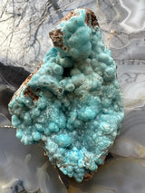 Blue botryoidal hemimorphite mineral specimen with rounded bubbly formations and patches of brown matrix rock, shown against a marbled agate background.