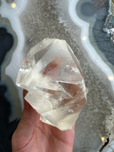 Translucent golden calcite crystal with angular facets held against a background of light gray and blue agate with concentric banding patterns.