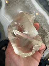 Translucent golden calcite crystal held in a hand, showing its angular facets and smooth, glassy surfaces with internal striations and reflections.