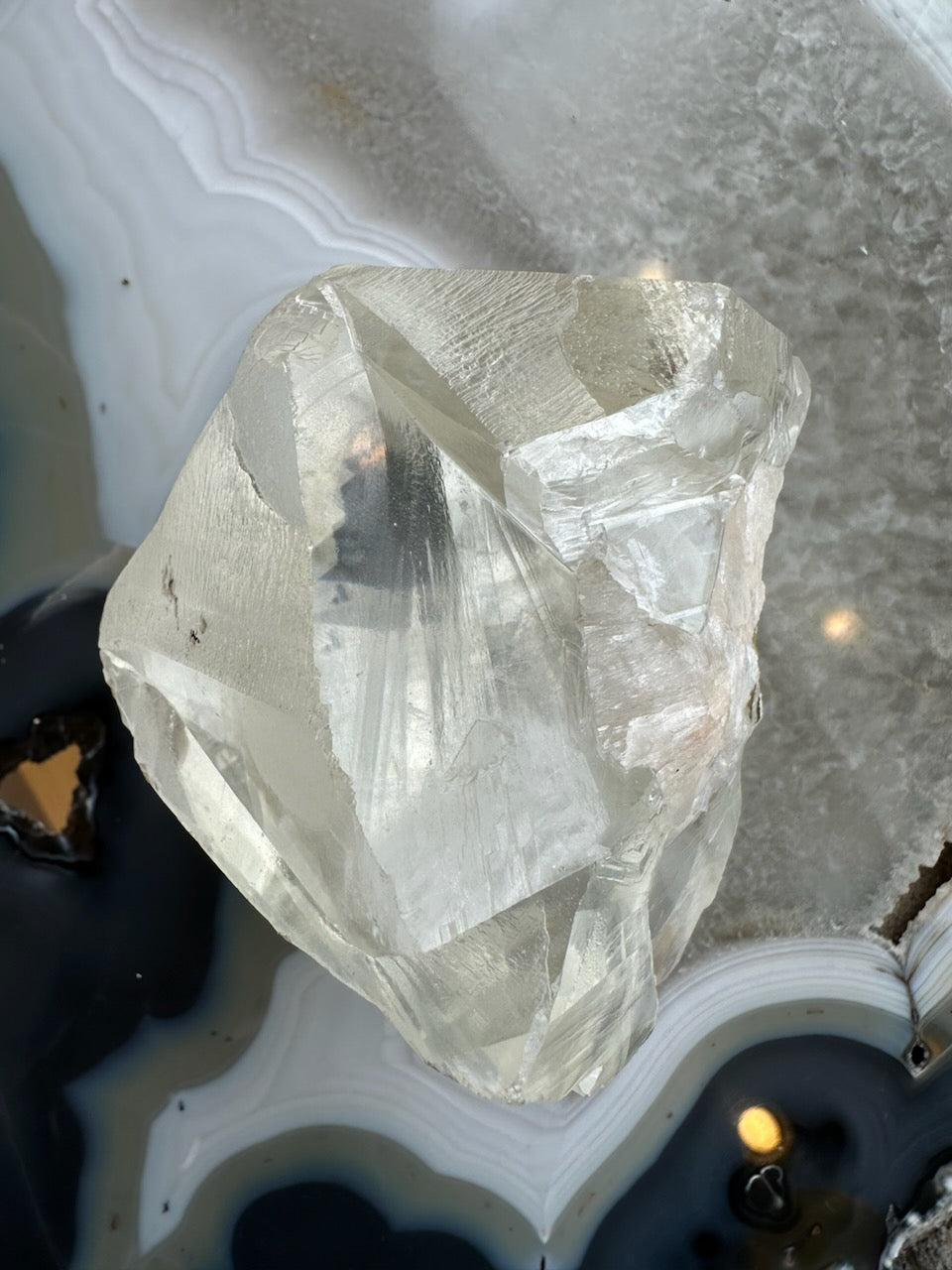 Translucent golden calcite crystal with sharp angular facets sitting on a polished agate slice featuring concentric gray, white, and black bands.