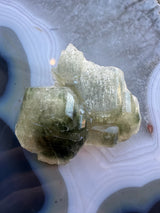 Translucent pale green fluorapatite crystal cluster with rectangular formations resting on a banded, blue and gray agate slice.