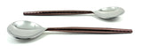 Two stainless steel tablespoons with hammered dark brown handles and smooth polished silver bowls, arranged parallel on a white background.