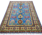 Rectangular hand-knotted Afghani Kazak wool rug with a blue central field featuring red and yellow star motifs and a beige border with geometric patterns and fringes