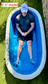Top view of a person wearing a white cap and dark clothes sitting inside a bright blue inflatable tub with a white rim on green grass outdoors.