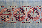 Section of a hand-knotted Afghani Kazak wool rug with repeating octagonal medallions in red, dark blue, and ivory on a light blue field, featuring geometric motifs.