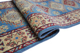 Close-up of a rolled Afghani Kazak wool rug with geometric star motifs in red, beige, and blue on a light blue background and detailed red borders.