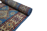 Partially rolled hand-knotted Afghani Kazak wool rug featuring geometric star and floral motifs in blue, cream, red, and beige tones with a detailed patterned border.