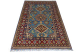 Afghani Kazak wool rug with a blue central field featuring geometric diamond motifs, bordered by intricate patterns in red, cream, and gold with multicolor fringe.