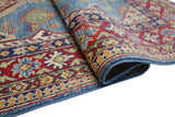 Close-up view of a hand-knotted Afghani Kazak wool rug featuring geometric patterns in red, blue, yellow, and green with a slightly rolled corner.