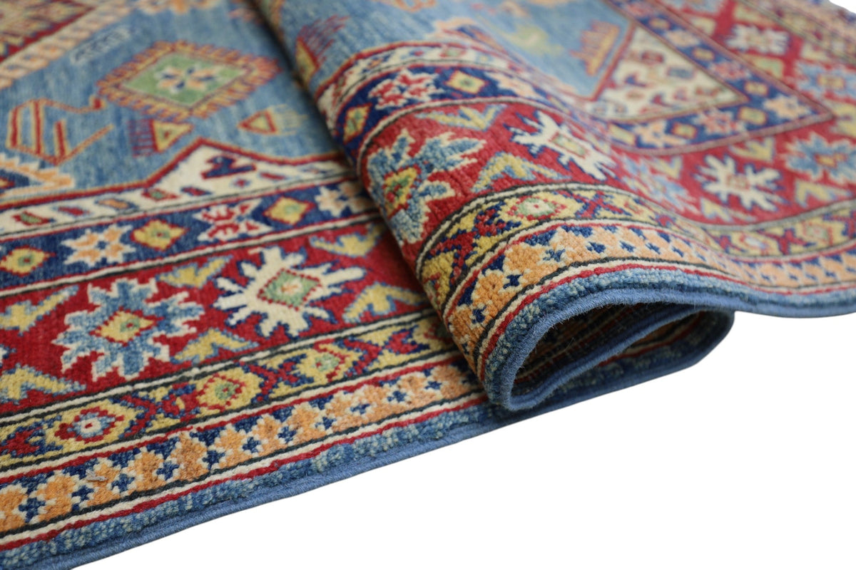 Close-up view of a hand-knotted Afghani Kazak wool rug featuring geometric patterns in red, blue, yellow, and green with a slightly rolled corner.