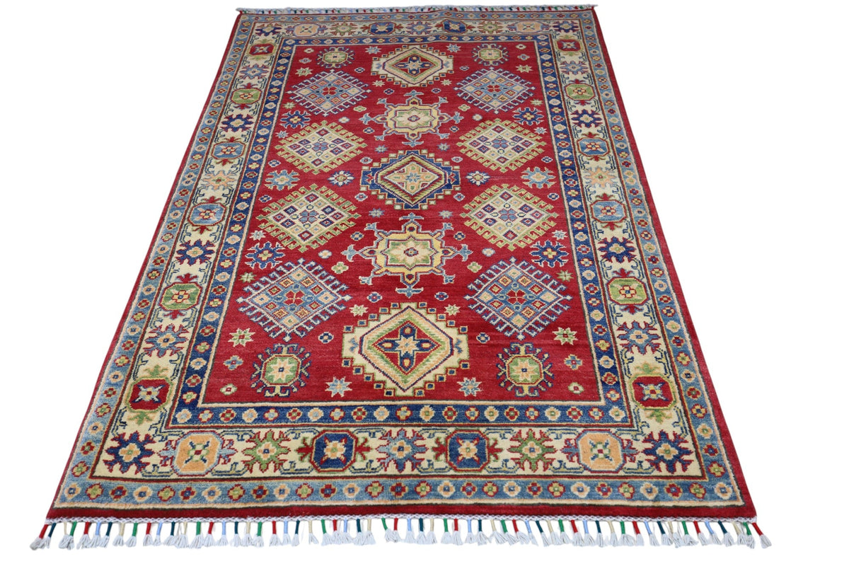 Rectangular hand-knotted Afghani Kazak wool rug with a rich red field featuring geometric medallions and a blue and cream floral border, fringed ends visible.