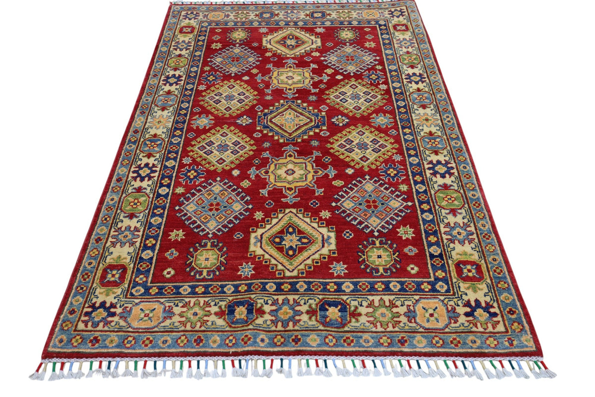 Rectangular Afghani Kazak wool rug with deep red field, geometric medallions, multi-colored floral motifs, and a wide beige and blue patterned border with fringe.
