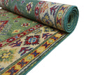 Partially rolled hand-knotted Afghani Kazak wool rug with green background, intricate multicolored geometric and floral borders, and detailed patterns in red, yellow, and blue.