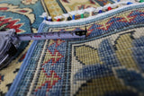 Close-up of a hand-knotted Afghani Kazak wool rug with yellow and red geometric patterns on a blue background, measured by a tape showing about 3 inches.