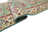 Close-up of a hand-knotted Afghani Kazak wool rug with a light turquoise background and intricate red, white, and blue geometric floral border patterns, partially folded.