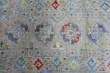 Wool rug with hand-knotted Afghani Kazak patterns in muted reds, blues, yellows, and greens on a beige background, featuring geometric medallions and borders.