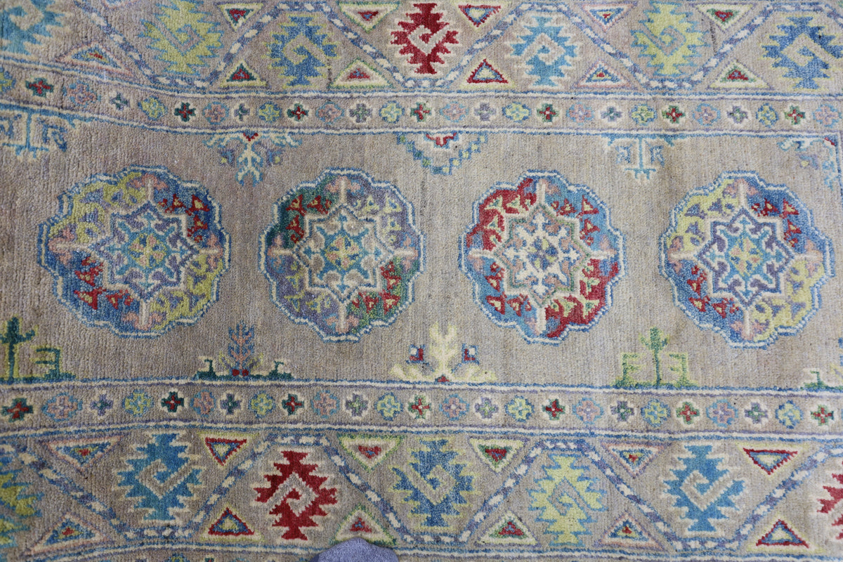 Wool rug with hand-knotted Afghani Kazak patterns in muted reds, blues, yellows, and greens on a beige background, featuring geometric medallions and borders.