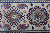 Close-up of a hand-knotted Afghani Kazak wool rug with geometric medallions in red, blue, green, and cream on a cream background.