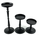 Set of three black metal pillar candle holders in varying heights with round trays and turned spindle-style stems on flat circular bases.