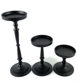 Set of three black pillar candle holders with round bases and trays, varying in height and featuring turned spindle-style stems on a white background.