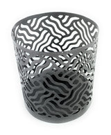 Grey metal votive candle holder with an intricate wavy cutout pattern forming abstract shapes around its cylindrical body.