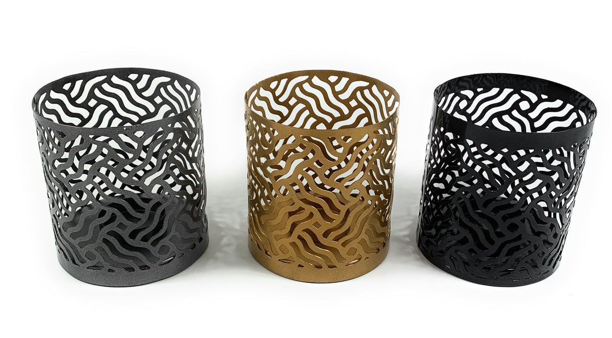 Set of three cylindrical votive candle holders with intricate maze-like cutout patterns in matte gray, gold, and black finishes on a white background.