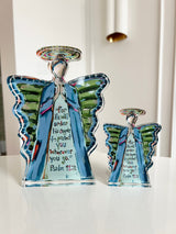 Two transparent acrylic angel figurines with multicolored wings and halos, each inscribed with Psalm 91:11 in stylized letters, displayed on a white surface indoors.