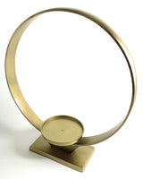 Minimalist circular gold metal candle holder with a flat round tray at the base, supported by a rectangular stand, shown on a white background.