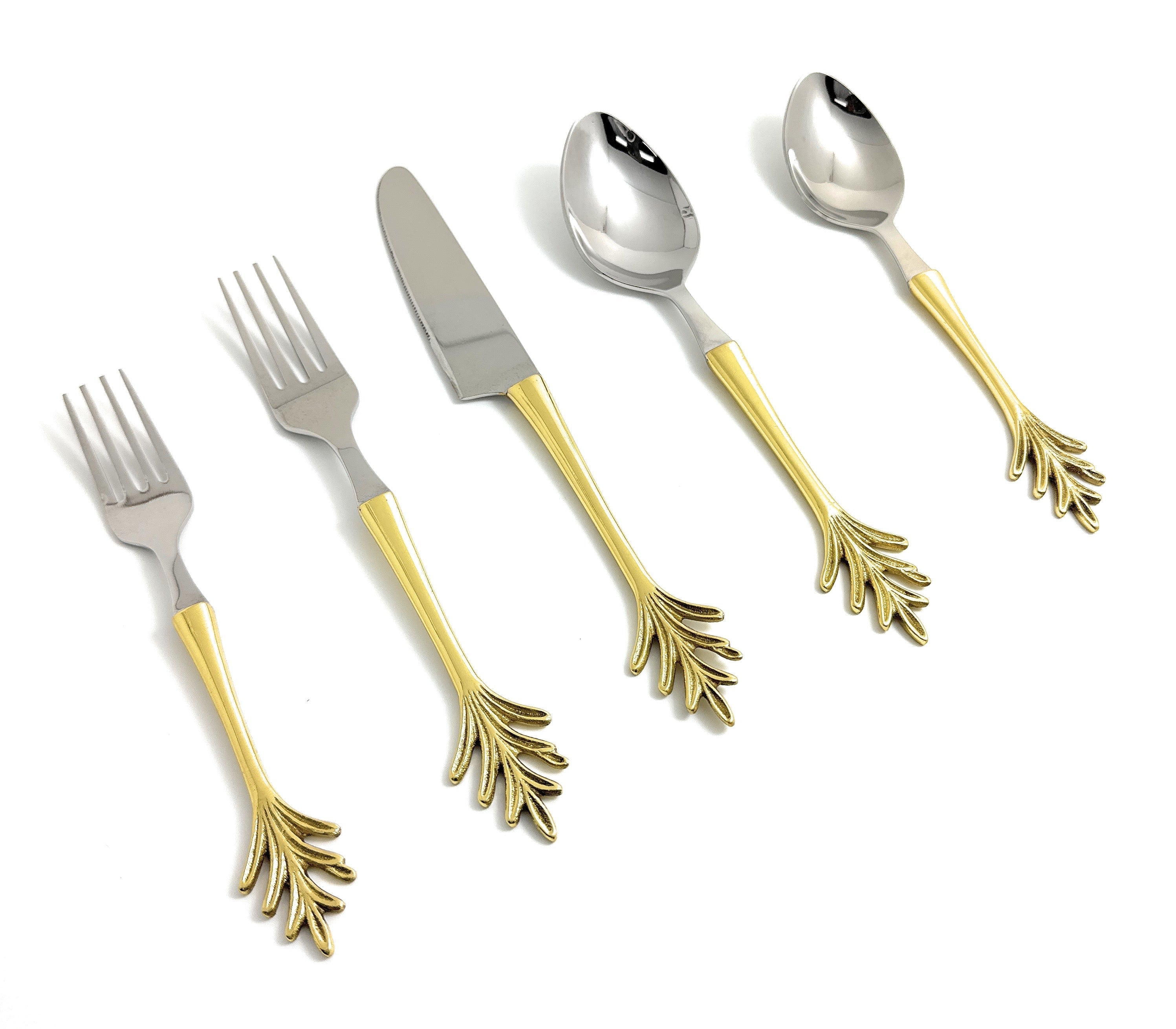 Golden flatware set with leaf style handles arranged on a dark table with natural decor accents