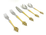 Five-piece flatware set with stainless steel heads and gold-colored handles featuring a decorative leaf motif at the ends, arranged on a white background.