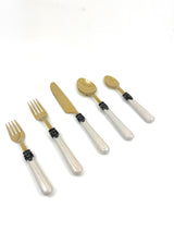 Set of white resin handle flatware including forks, knives, and spoons arranged on a cloth napkin with wine glasses nearby.