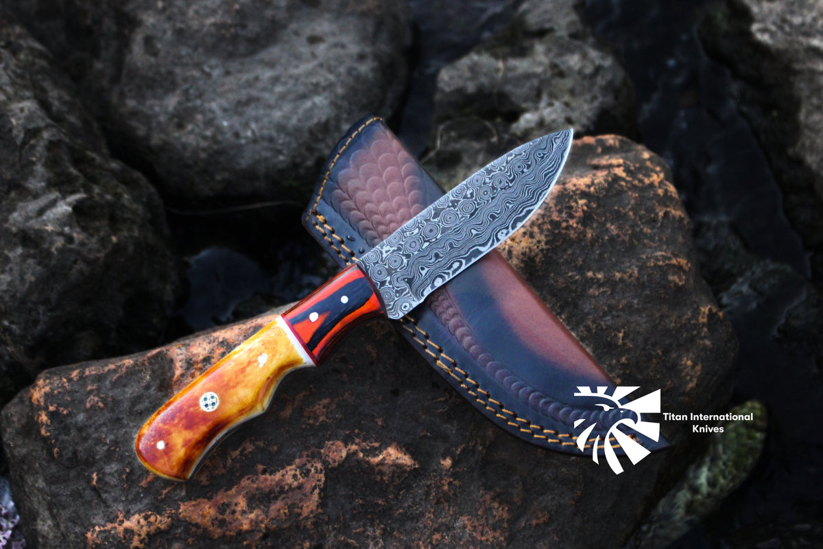 Custom /Titan Spade/ Damascus Steel Hunting Knife with burnt bone and diamond wood handle resting on wood surface with leather sheath