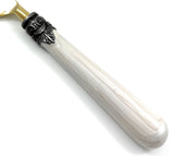 Close-up of a white resin flatware handle with a glossy finish, featuring an ornate black collar detail near the brass-toned utensil base.
