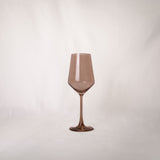 Single translucent brown-tinted wine glass with a long stem and slightly angular bowl shape on a white background.
