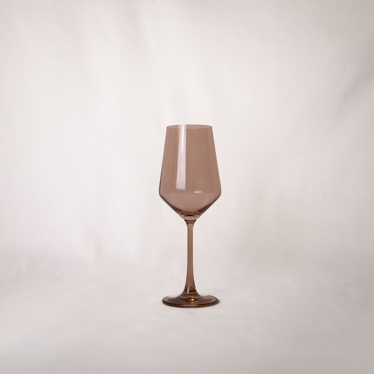 Single translucent brown-tinted wine glass with a long stem and slightly angular bowl shape on a white background.