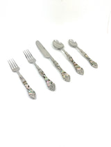 Stainless steel flatware pieces with seashell and wave patterned handles laid out on a surface