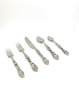 Flatware set with abalone shell-patterned handles including two forks, one knife, and two spoons arranged on white background.