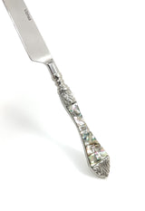 Stainless steel butter knife with an ornate handle featuring iridescent abalone shell inlay and intricate silver floral detailing at the ends.