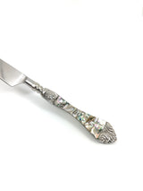 Butter knife with a stainless steel blade and a handle featuring iridescent abalone shell inlays and ornate silver floral engravings at both ends.
